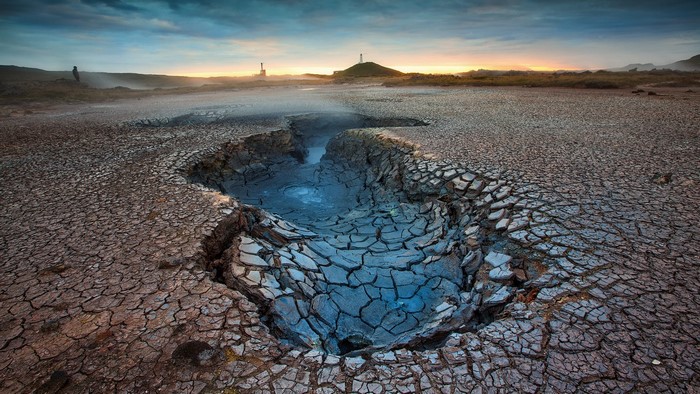 Cracked earth and mud pool landscape with distant structures