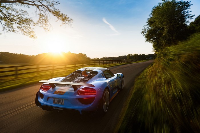 Blue Porsche 918 Gulf driving on a country road at sunset
