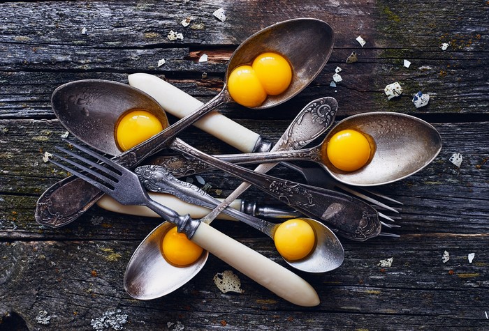Egg yolks in antique spoons and forks on wooden table