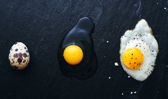 Quail egg, raw egg, and fried egg on black slate