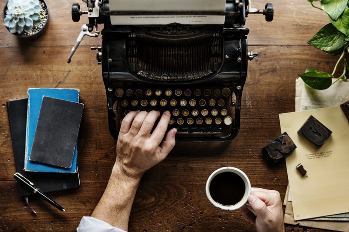 Hands typing on a vintage typewriter with coffee and books