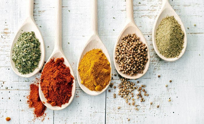 Wooden spoons filled with colorful spices on a white wooden surface