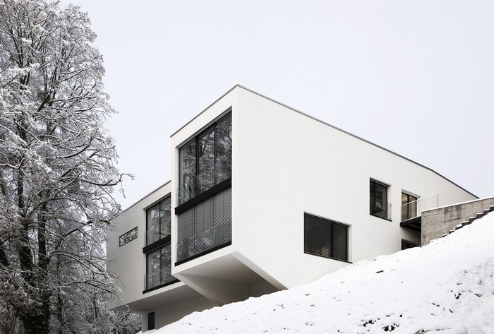Modern white house covered in snow with trees