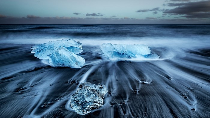 Ice chunks on a black sand beach with ocean waves