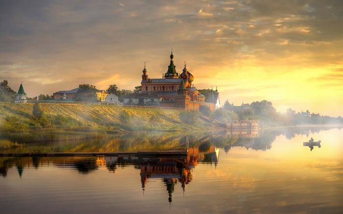 Monastery on a riverbank at sunrise with a boat