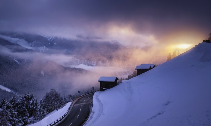 Snowy mountain road with cabins and fog