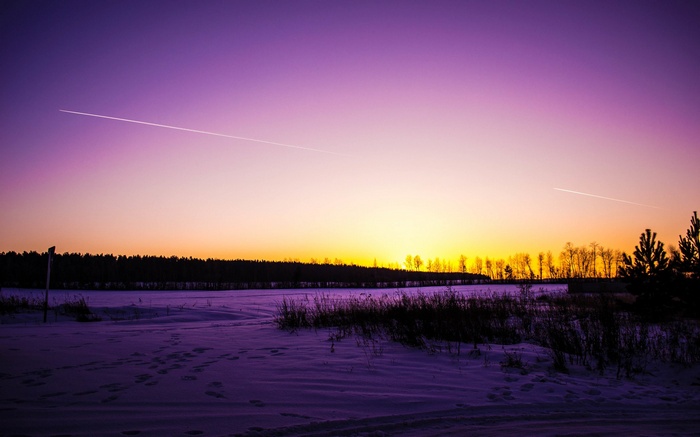 Airplane contrail over a snowy landscape at sunset