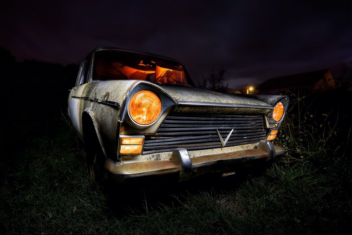 Old rusty car with glowing headlights at night