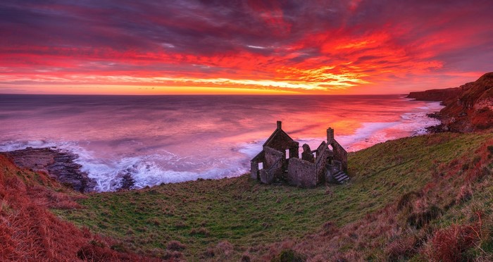 Ruined house on a cliff overlooking the ocean at sunset