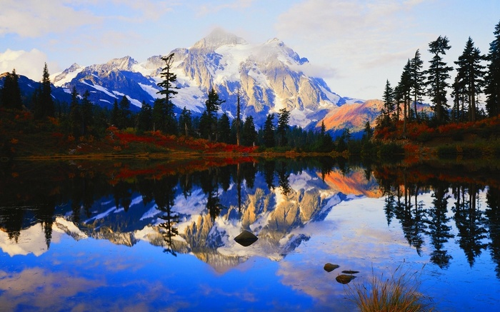 Snow-capped mountain reflected in a calm lake with pine trees