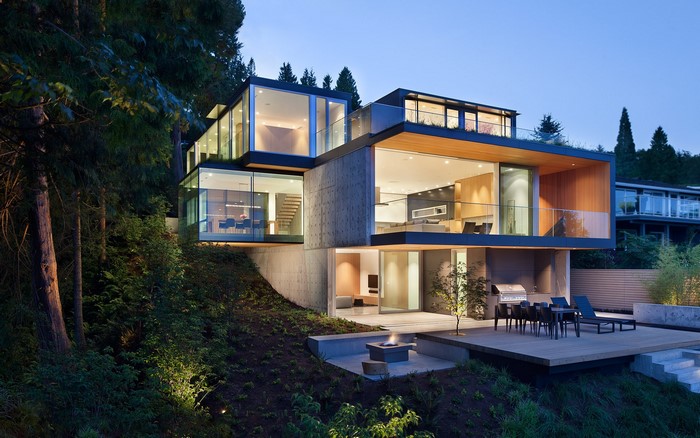 Modern multi-story house with glass walls on a wooded slope