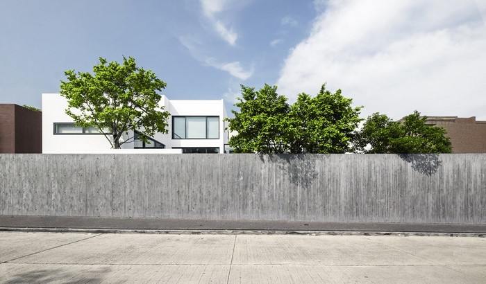 Modern white house behind a concrete wall with trees