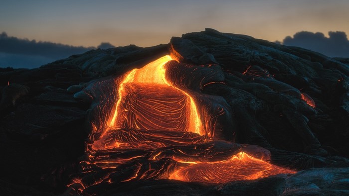 Molten lava flowing over dark volcanic rock at dusk