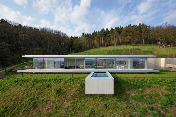 Modern glass house with swimming pool on a grassy hill