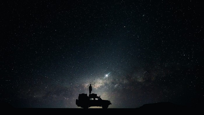 Silhouette of a person on a car under the Milky Way