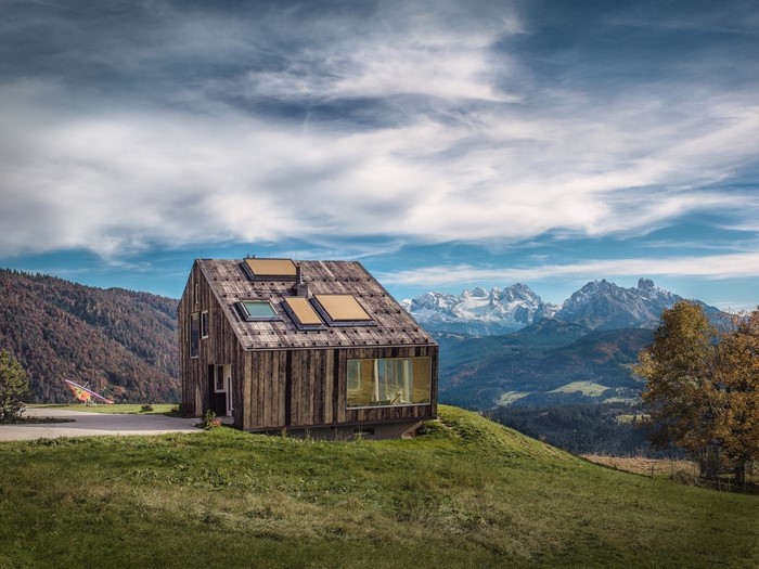 Modern wooden house on a grassy hill with mountains
