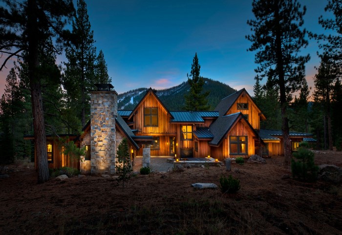 Modern wooden house with stone chimney in a forest at dusk