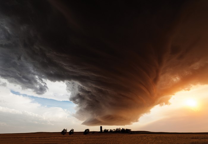 Tornado storm over a field with trees and a silo