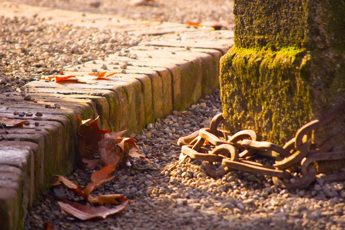 Rusty chain near mossy stone and brick border
