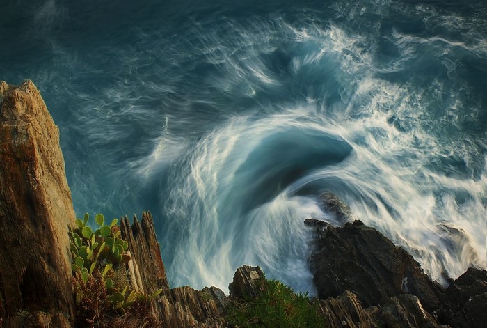 Long exposure of waves crashing on rocks with cactus