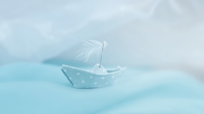 A small blue polka dot paper boat with a feather sail