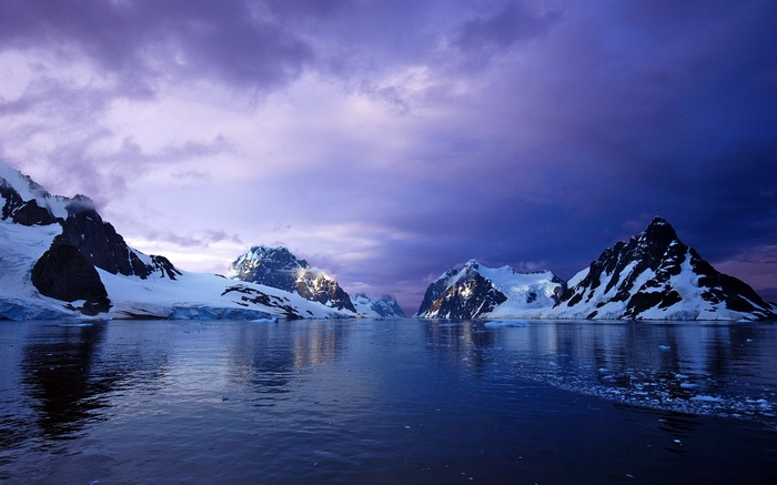 Snow-capped mountains reflected in calm water under a purple sky