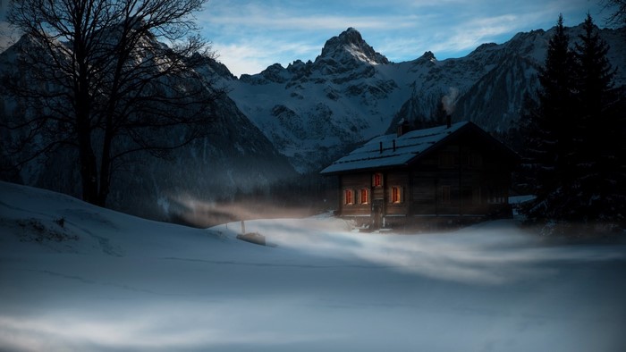Wooden cabin in snowy mountains at dusk with mist