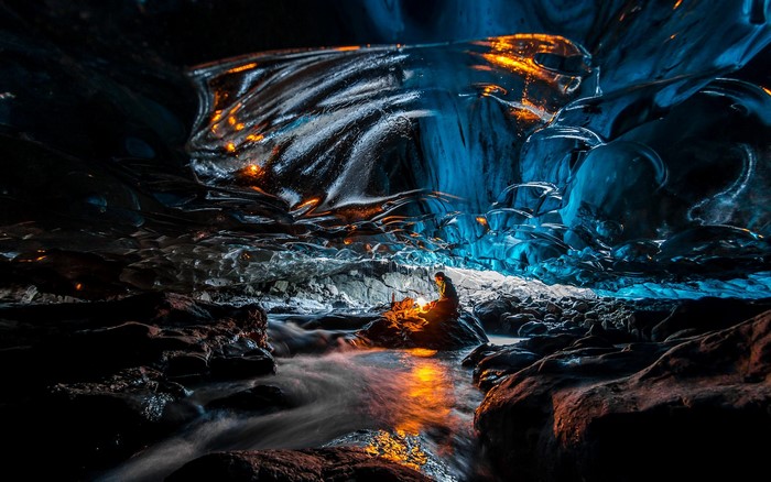 Person sitting by stream in ice cave with orange light