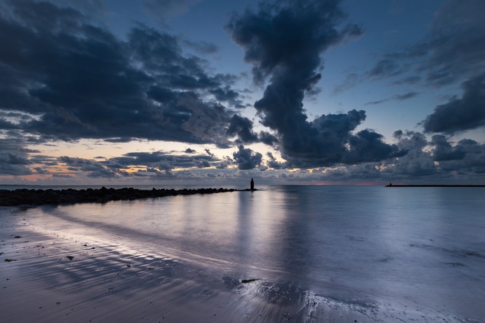 Dark clouds over a calm sea at dusk with a lighthouse