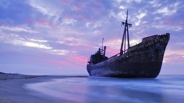 Shipwreck on a beach at sunset with violet clouds