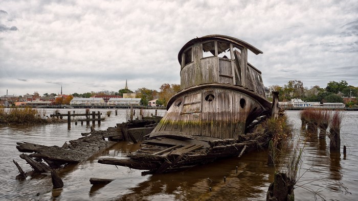 Abandoned shipwreck in a river with cityscape background