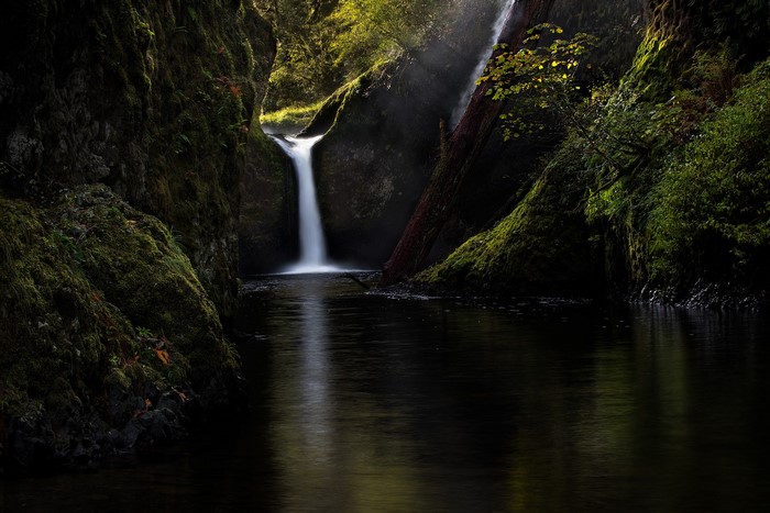 Waterfall cascading into a dark pool surrounded by mossy rocks