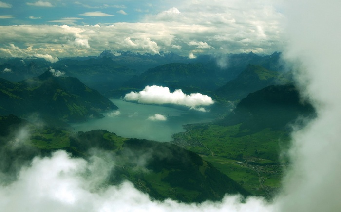 Aerial view of a lake surrounded by green mountains and clouds