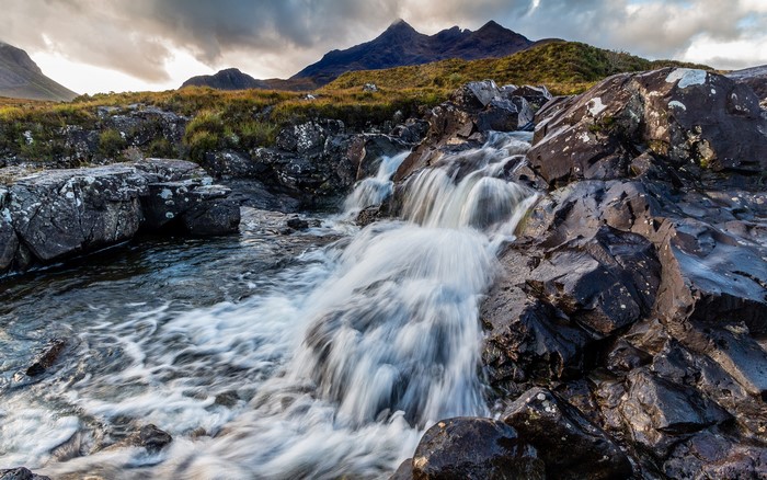 Waterfall flowing over rocks with mountains in the background