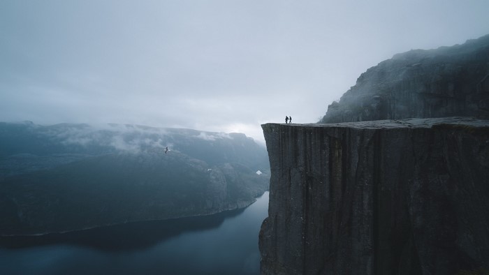 Two people stand on a cliff overlooking a fjord in Norway