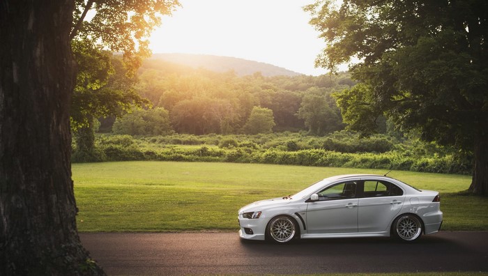 White Mitsubishi Lancer Evolution parked on a road with trees and hills