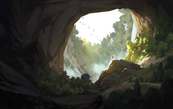 A person stands on a rock overlooking a sunlit cave entrance