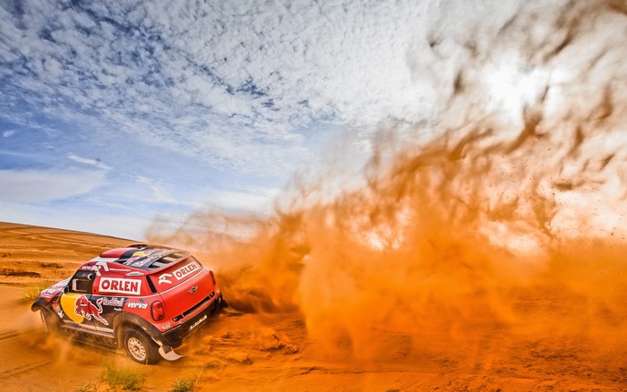 Red Mini Cooper rally car kicking up sand