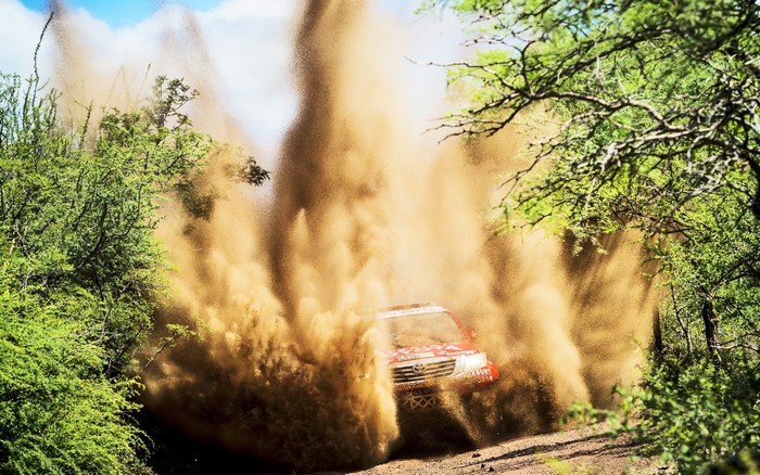 Red Toyota rally car kicking up dust on a dirt road