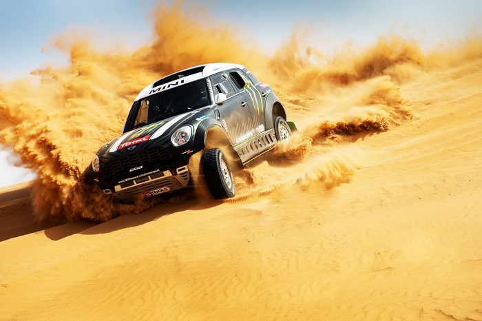 Mini Cooper rally car racing through desert sand dunes