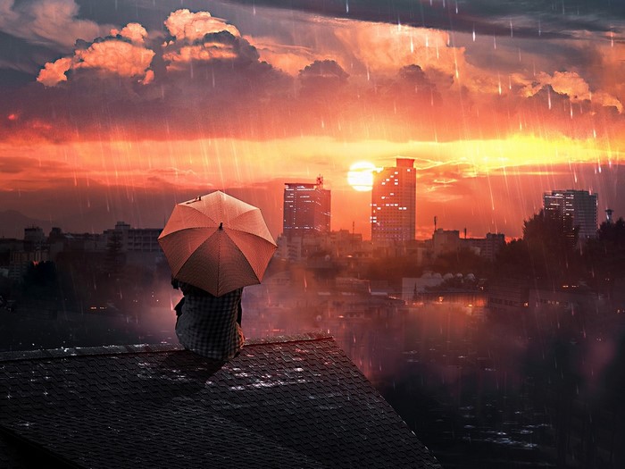 Person with umbrella on rooftop during rain at sunset