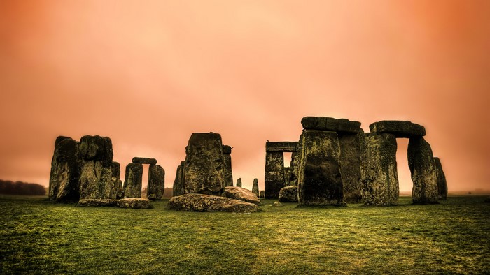 Stonehenge ancient monument on grassy field under orange sky