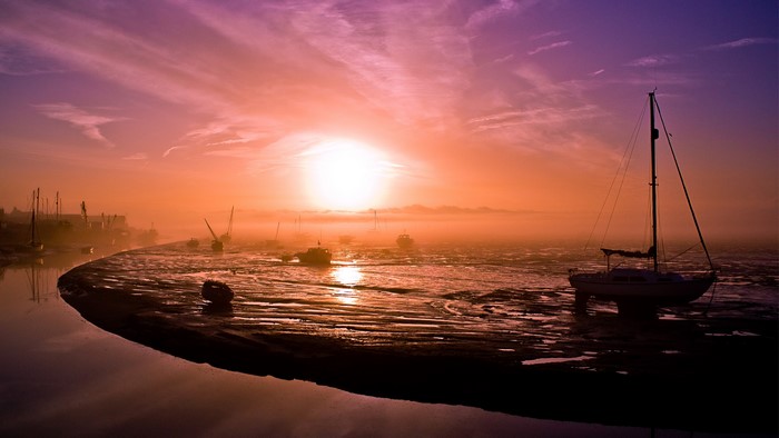 Boats in foggy sunrise over water