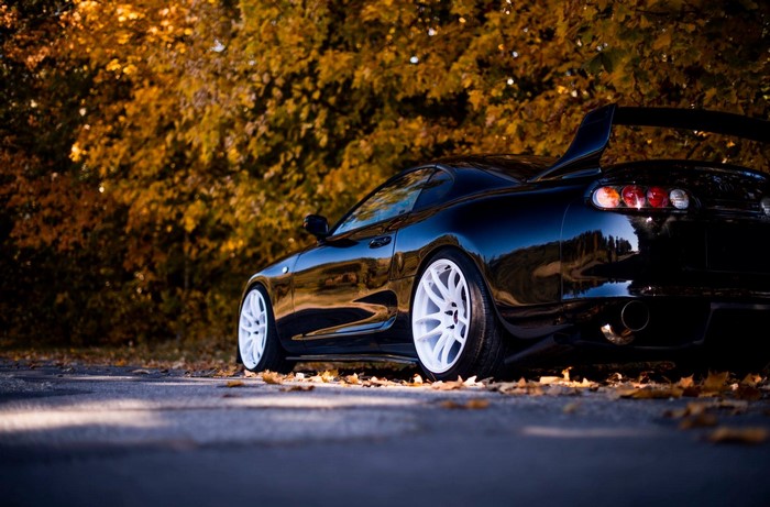 Black Toyota Supra with white wheels in fall