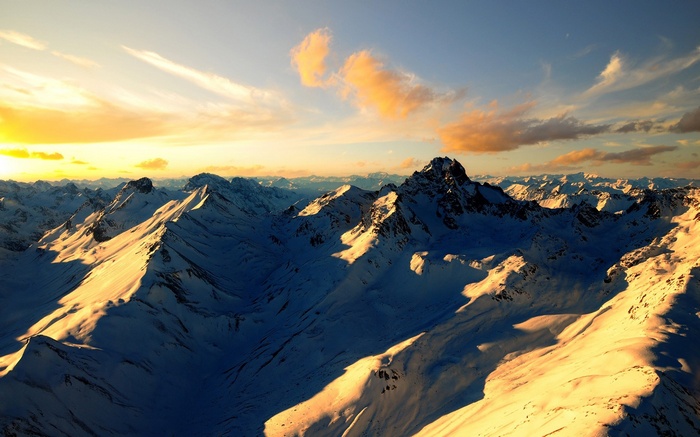 Snowy mountain range at sunset with golden clouds