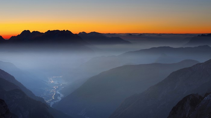 Misty valley at sunset with orange sky and mountains
