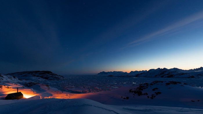 Cabin with lights in snowy Greenland landscape at dusk