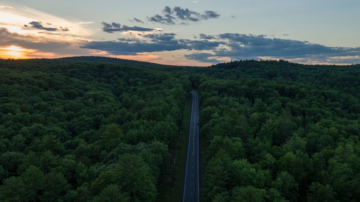 Aerial view of a highway through a forest at sunset
