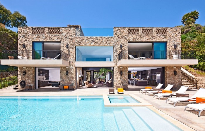 Modern stone mansion with swimming pool and lounge chairs
