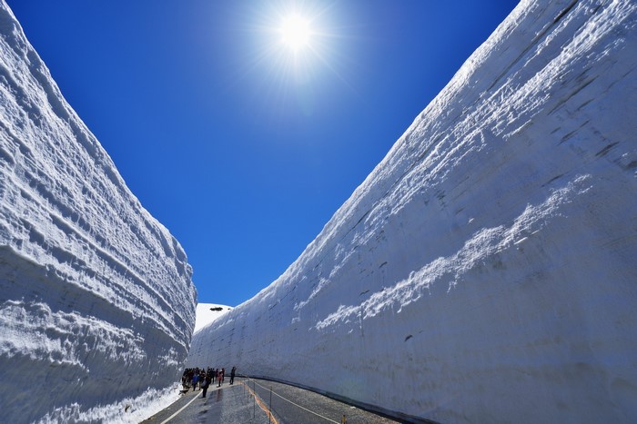 Snow walls and people on a road under the sun in Japan